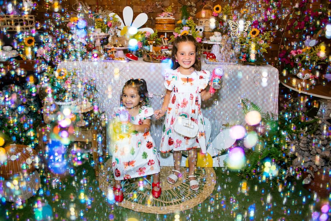Duas meninas cercadas de bolhas de sabão diante da mesa decorada